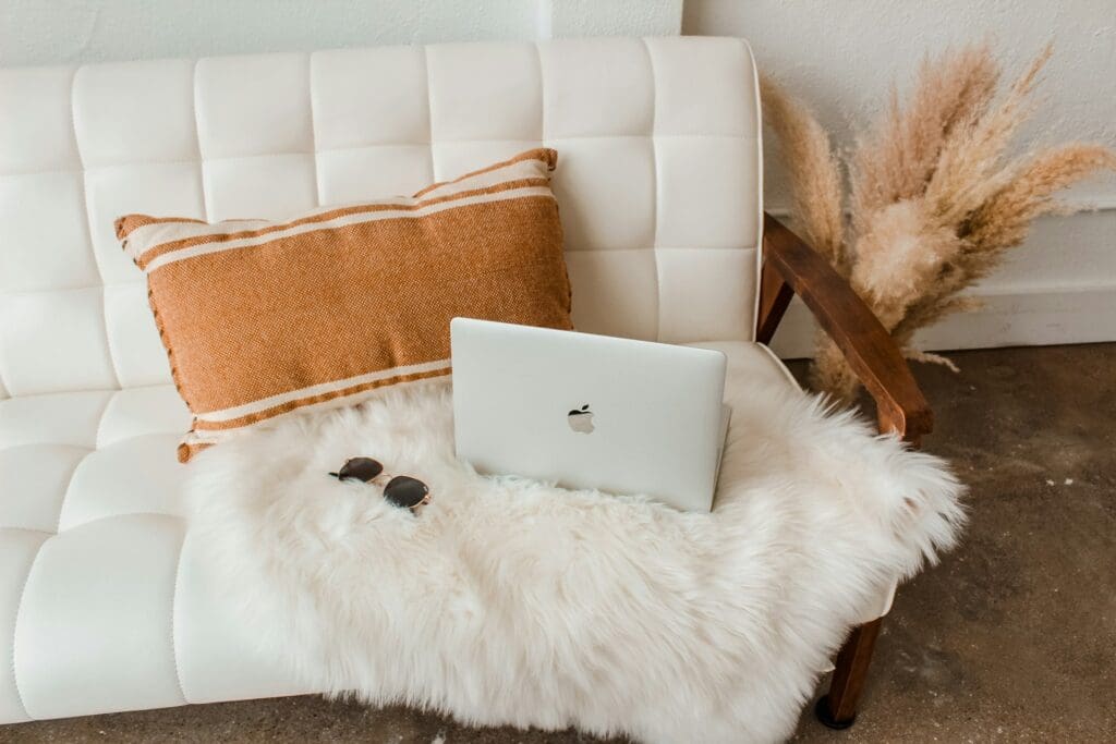 laptop on a decorated white couch with an orange pillow.